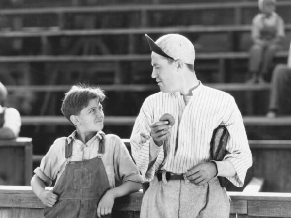 Older photograph of a man at a baseball, mentoring a boy