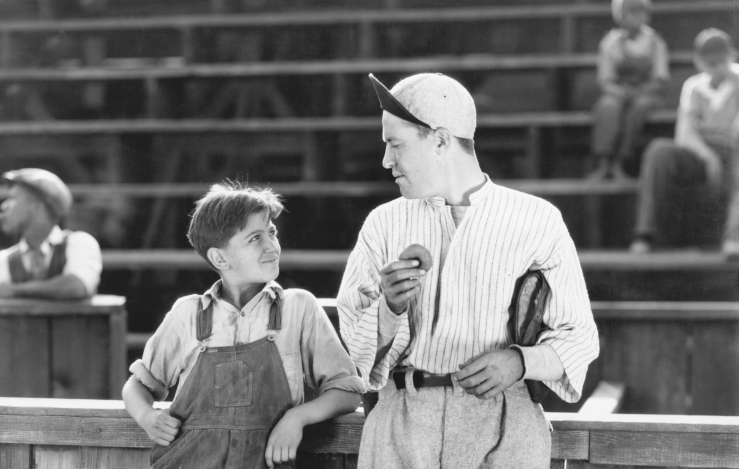 Older photograph of a man at a baseball, mentoring a boy