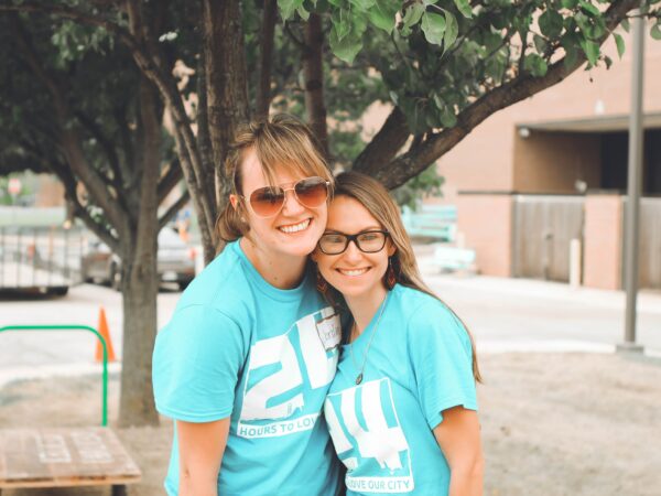 two women embracing each other, wearing blue big brothers big sisters volunteer shirts